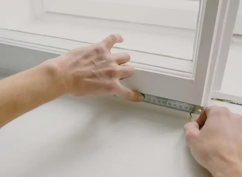 A professional installer using a measuring tape to accurately measure the width and height of a window for custom windows treatment.